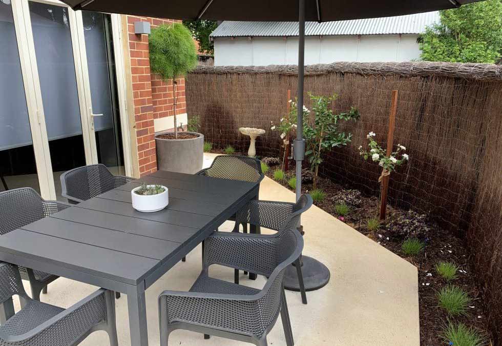 Image of an example of a simple front garden idea with small patio and grey table, chairs and parasol